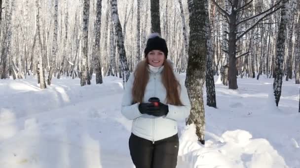 Glada leende kvinna med kopp varmt kaffe eller te utomhus på vintern i skogen — Stockvideo