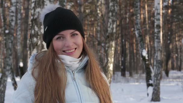 Крупный план красивой девушки, улыбающейся, глядя в камеру в зимнем лесу. Обезжиренный фон в зимнем лесу — стоковое видео