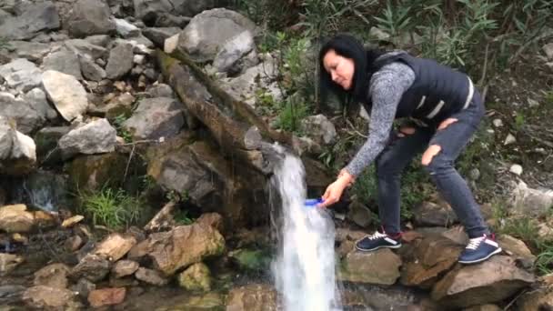 Eine Frau sammelt Wasser aus einer Bergquelle. Sauberes Trinkwasser ist hoch in den Bergen. Wasserfall aus reinem Süßwasser im Wald. — Stockvideo