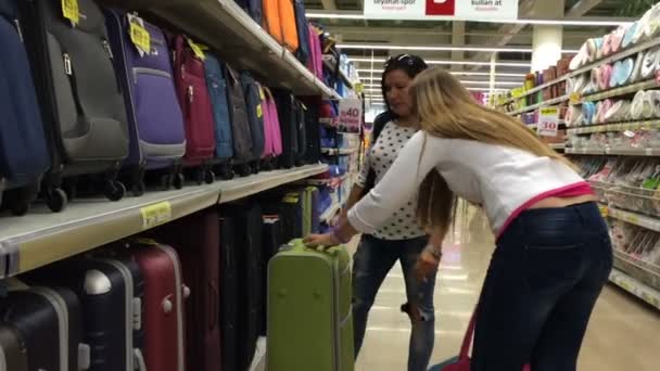 Twee vrouwen in een supermarkt te kopen van een koffer. Selecteer en nemen een koffer te slaan rekken. — Stockvideo