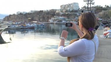 Genç kadın bir fotoğraf historyc gemisi günbatımında yapıyor. Akıllı telefon ile beyaz kız manzara fotoğraf günbatımı, Akdeniz sahilinde ayakta yapar. Portre. HD 1920 x 1080