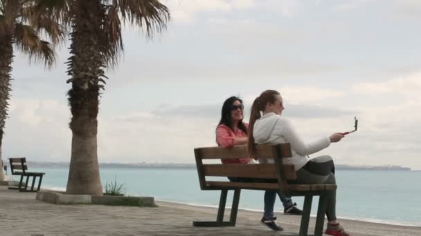 Two Young woman taking self portrait sitting on the seafront using smartphone mobile cell phone camera. Closeup. HD 1920x1080. — Stock Video