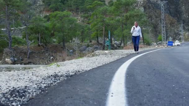 Mooie jonge vrouw lopen op de weg houden van een slimme telefoon en glimlachen — Stockvideo