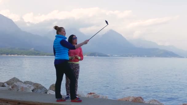 Mama și fiica sunt fotografiate pe un smartphone în fundalul mării și al munților în timpul verii. — Videoclip de stoc