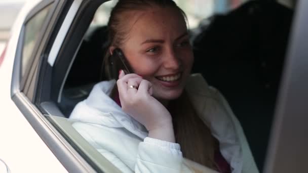 Γκρο πλαν του όμορφη ευτυχισμένη κοπέλα χρησιμοποιεί να μιλήσουμε smartphone που κάθεται στο πίσω κάθισμα του αυτοκινήτου — Αρχείο Βίντεο
