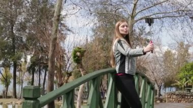 Kendi kendine portre ayakta smartphone cep telefonu kamera ile ahşap Köprü'alarak genç mutlu bir kadın. Portre. HD 1920 x 1080.