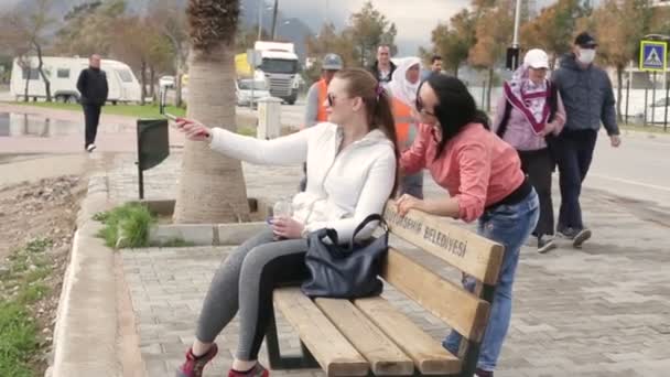 Két fiatal nő ül a tengerparton használ smartphone mozgatható sejt telefon fényképezőgép önarckép figyelembe. — Stock videók