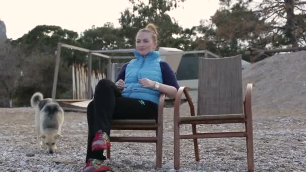 カメラを見て、若い女性を美しいビーチでの木製のベンチに座って. — ストック動画
