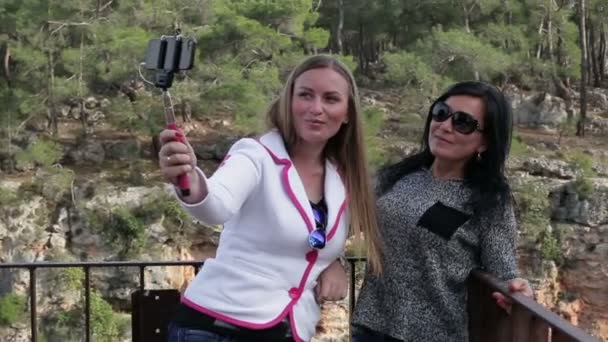 Dos mujeres hermosas jóvenes que se fotografian usando un teléfono inteligente en la calle en el parque — Vídeo de stock