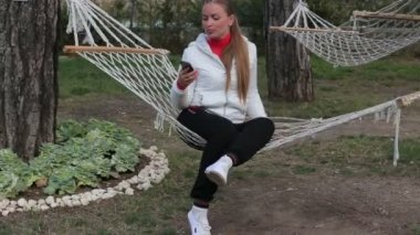 Güzel genç kız hamak gülümseyerek oturan bir akıllı telefon kullanmak için söz
