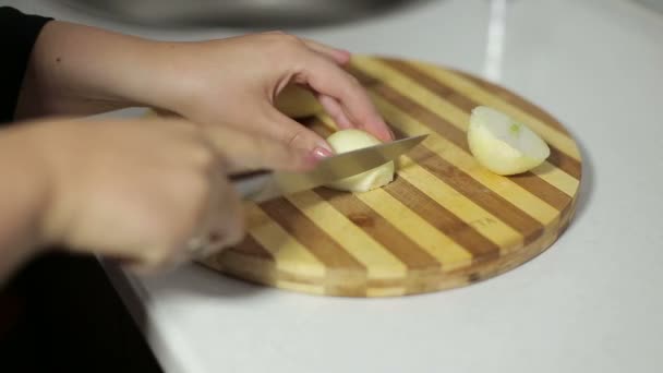 Mano femenina con un cuchillo cortado cebollas en una tabla de cortar — Vídeo de stock