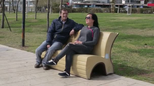 Любителі чоловік і жінка розмовляють, сидячи на лавці парку — стокове відео