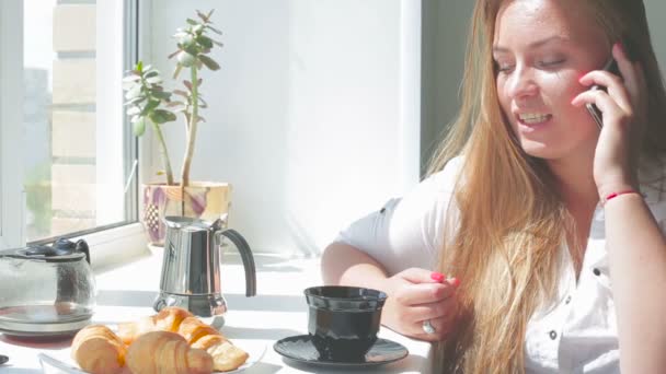 Joven hermosa chica tiene el desayuno uso de teléfono inteligente en un día soleado — Vídeo de stock