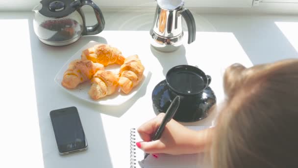 Unga vackra flicka har frukost skriver ett brev i en anteckningsbok på en solig dag — Stockvideo