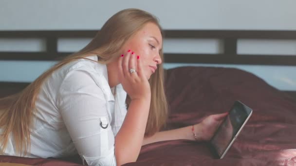 Hermosa chica joven acostada en la cama y el uso de tableta sonriendo — Vídeos de Stock