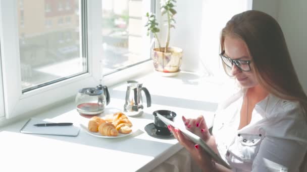 Молодая красивая девушка завтракает планшетным компьютером в солнечный день — стоковое видео