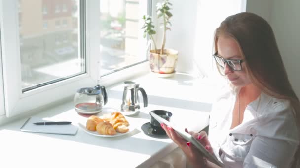 Joven hermosa chica tiene desayuno uso tableta ordenador en un día soleado — Vídeos de Stock