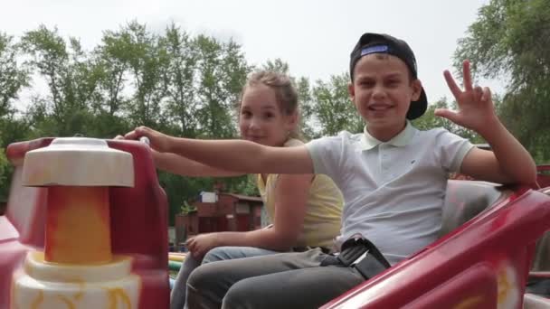 Dos niños alegres se preparan para un viaje a la atracción, agitando las manos y riendo — Vídeos de Stock