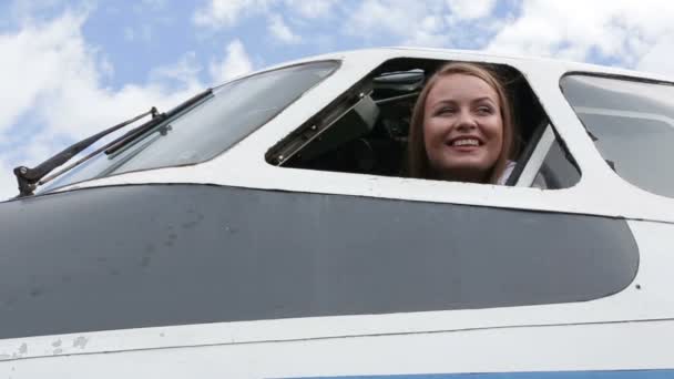 Belle jeune fille pilote assise aux commandes d'un avion, regarde par la fenêtre — Video