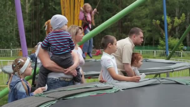 Kurgan, Russia - July 2016: people stand side by side in the park, children jumping on the trampoline — Stock Video