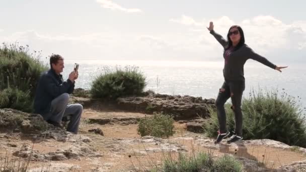 Hombre uso smartphone fotografiando mujer de pie sobre una roca — Vídeo de stock