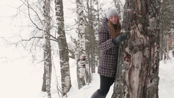 Una mujer joven caminando en el bosque de invierno y abrazando un árbol — Vídeos de Stock