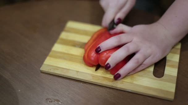 Close-up een handen van een jonge vrouw die hakken van groenten op een houten bord. — Stockvideo