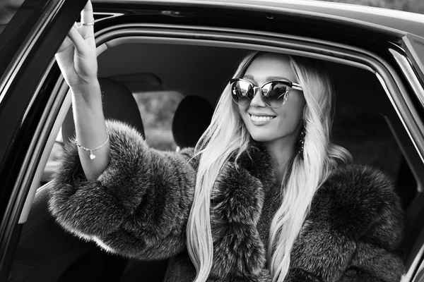 Sexy woman with long blond hair in casual clothes and fur posing beside luxurious car — Stock Photo, Image
