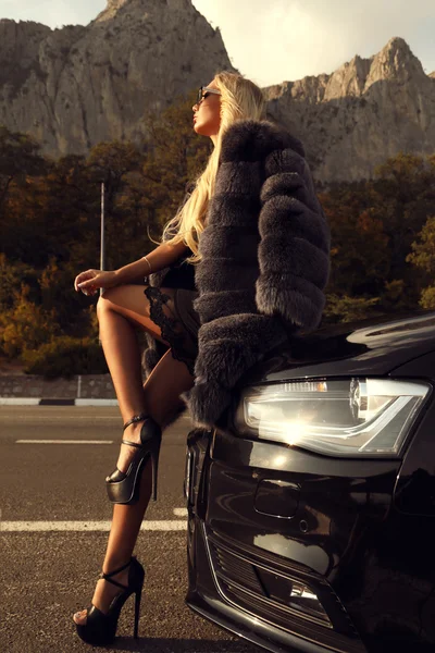 Femeie sexy cu păr lung blond în haine casual și blană pozând lângă mașina de lux — Fotografie, imagine de stoc
