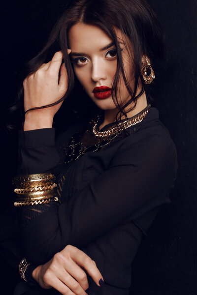Fashion studio portrait of gorgeous woman with dark hair and bright makeup with luxurious bijou, massive necklace and bracelets