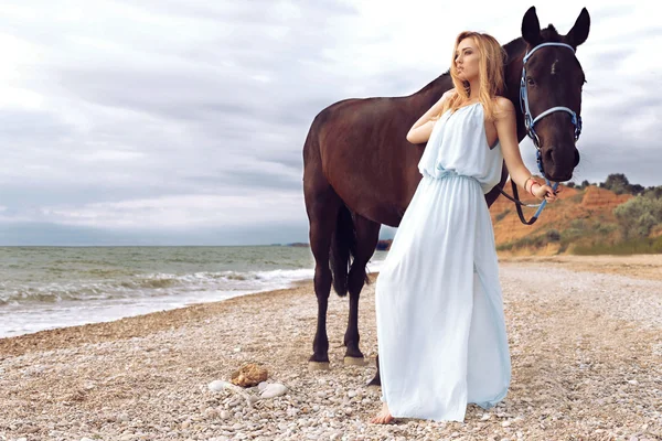 Jovem loira mulher com cavalo preto — Fotografia de Stock