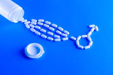 Erectile dysfunction therapy medical concept. Pills are poured out of a bottle and stacked in a male gender symbol on a blue background clipart