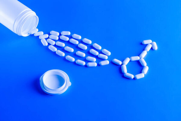Erectile dysfunction therapy medical concept. Pills are poured out of a bottle and stacked in a male gender symbol on a blue background