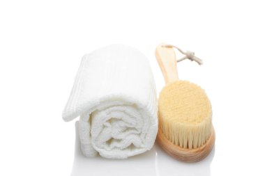 Doğal malzemelerden yapılmış kuru bir masaj fırçası ve beyaz arka planda bir pamuk havlu. Temizlik ve vücut bakımı kavramı