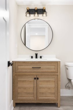 Beyaz meşe dolabında beyaz tezgahı olan, dairesel aynanın üzerinde siyah ve altın armatür ve bronzlaşmış duvarları olan modern bir çiftlik evi..