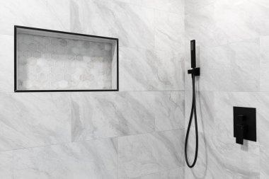 Mermer kiremit duvarlı bir banyo duşu, siyah musluk ve altıgen kaplama döşemeli bir raf..