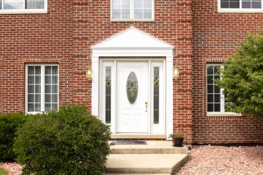 Beyaz kapılı, dairesel pencereli ve beyaz kapılı kırmızı tuğlalı bir evin ön kapısı..