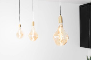 Modern minimalist bir iç mekanda tavandan sarkan sıcak kehribar rengi üç adet Edison tarzı ampul.