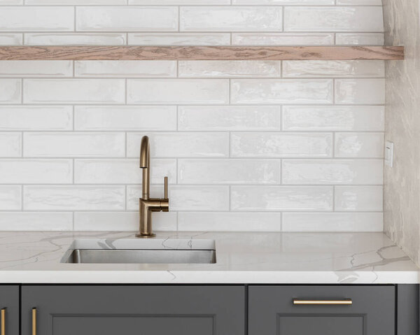 A modern kitchen sink detail with a brass faucet against a white subway tile backsplash, floating natural wood shelf, dark gray cabinets, and pattern wallpaper.