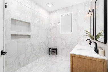 Dikey bronzlaşmış metro döşemesi, beyaz mermer tezgahı, yerde mermer döşemesi ve duşu olan beyaz meşe süsleme dolabı olan bir banyo detayı..