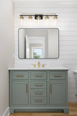 Altın donanımlı, ahşap döşemeli, modern bir banyo ve teknede aynanın üzerine monte edilmiş siyah ve altın renkli bir ışık..