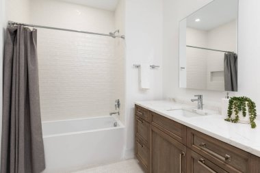 Ahşap bir dolapta mermer tezgahı olan lüks bir banyo, beyaz ringa kemiği döşemesi ve krem metro fayanslarıyla dolu bir duş..