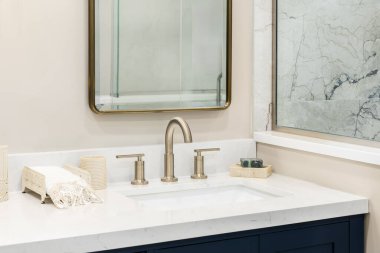 Mavi makyaj dolabında beyaz bir tezgahı olan bronz bir banyo musluğu ve mermer kaplama bir duş..