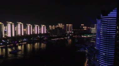 Gecenin hava manzarası Sanya Körfezi, Hainan Adası, Çin, 4k 'deki nehir kenarı apartmanını aydınlattı. 