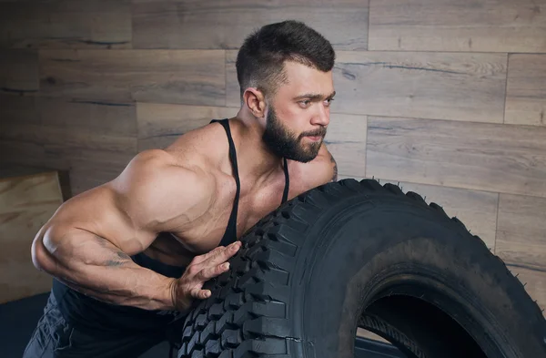 블랙 탱크 탑에는 타이어를 밀고 수염과 근육 질의 남자 — 스톡 사진
