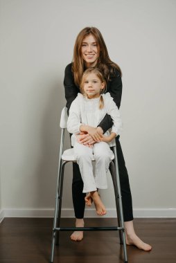 Genç ve güzel bir anne bar taburesinde oturan kızına sarılıyor. Gülümseyen bir anne ve mutlu bir sarışın çocuk poz veriyor.