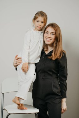 Bir anne bar taburesinde duran kızına sarılıyor. Gülümseyen bir anne ve mutlu bir sarışın çocuk poz veriyor.