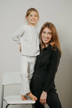 Genç bir anne bar taburesinde duran kızına sarılıyor. Gülümseyen bir anne ve mutlu bir sarışın çocuk poz veriyor.