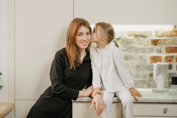 Uma Filha Loira Está Beijando Sua Jovem Mãe Bochecha Cozinha — Fotografia de Stock