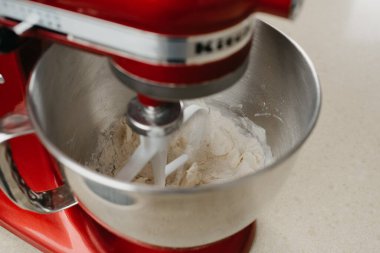 Tereyağı, badem unu ve buğday ununu bir mutfakta paslanmaz çelik karıştırma kabında kısayol hamur işine karıştıran kırmızı bir standın yakın bir fotoğrafı..